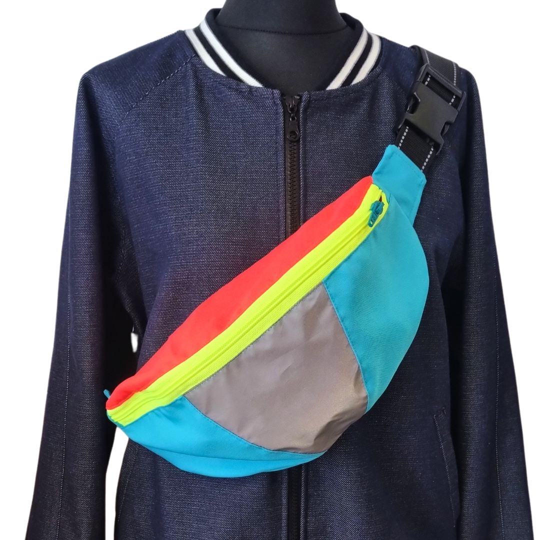 Crossbag in blau, rot und gelb mit Reflexelement schräg getragen auf einer Schneiderpuppe gezeigt.