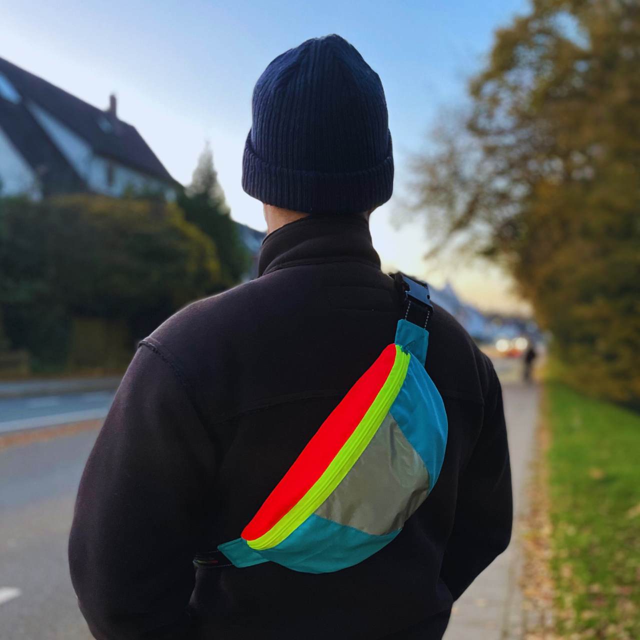 Bunte Crossbag in neongelb, neonrot und blau mit Reflexelement auf dem Rücken einer Person.