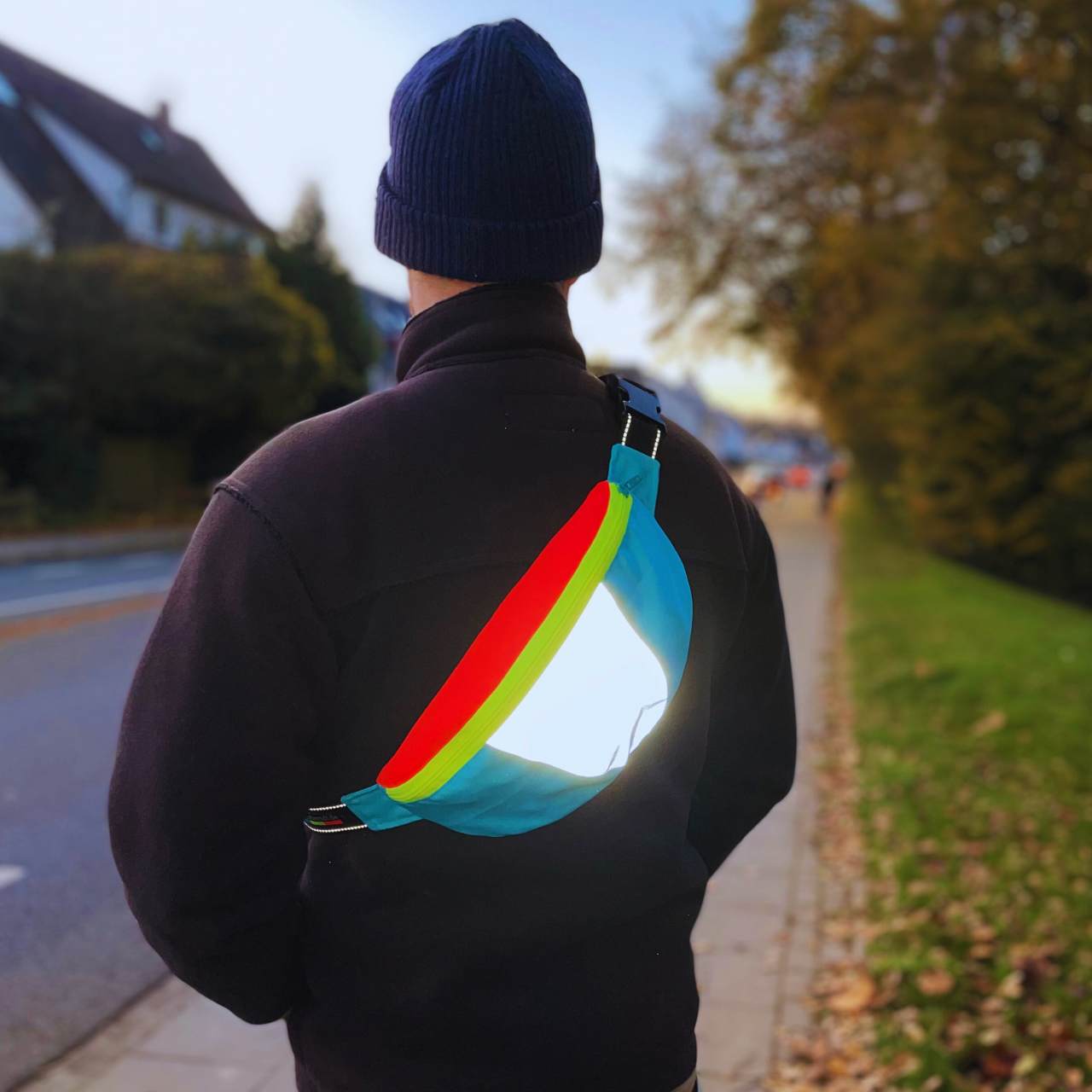 Crossbag in blau, neonrot und neongelb mit großem reflektierendem Element und schwarzem Gurtband mit Reflexstreifen.