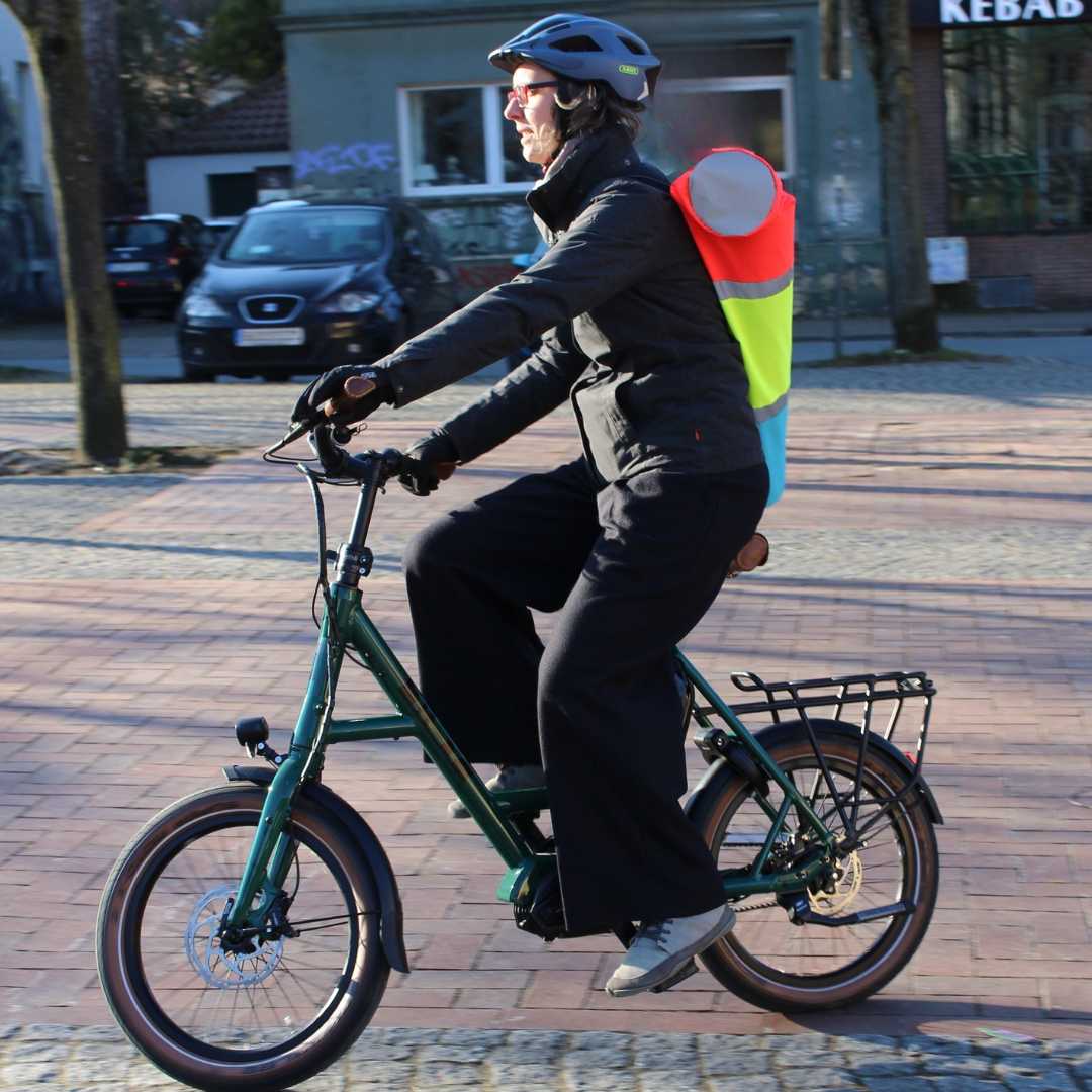 Frau auf Fahrrad mit bunter reflektierender Yogamattentasche.