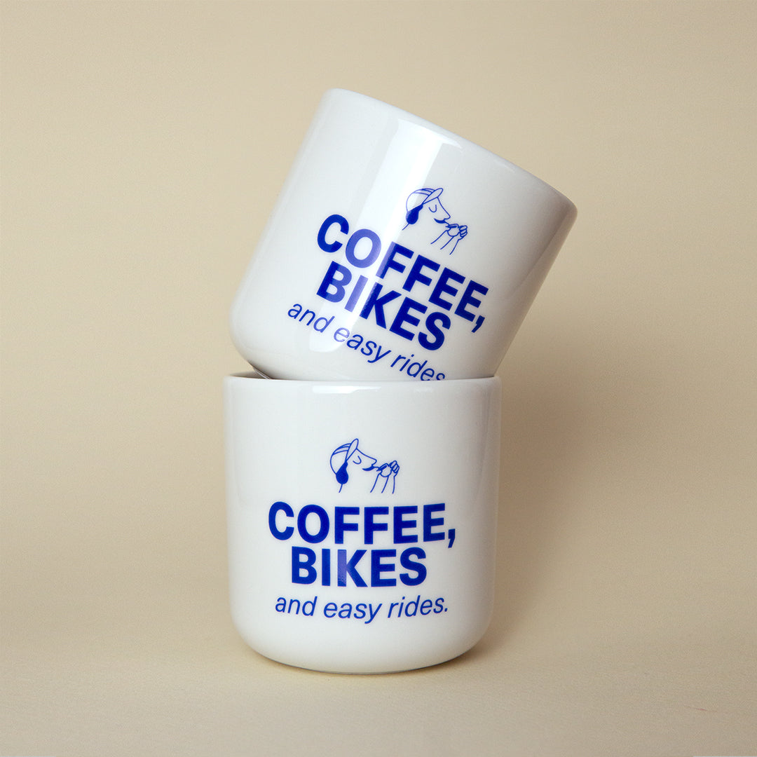 zwei aufeinandergestapelte Tassen mit blauem aufdruck: "Coffee, Bikes and easy rides"