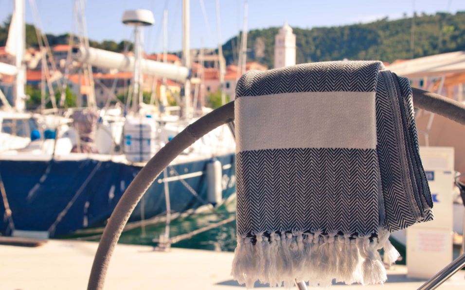Strandtuch von ecobain in schwarz-beige vor einer Hafenkulisse