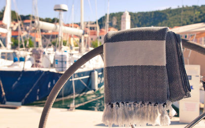 Strandtuch von ecobain in schwarz-beige vor einer Hafenkulisse