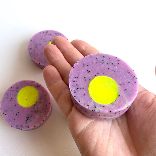 Seife Mathilda rund in lila und neon gelb auf Hand.